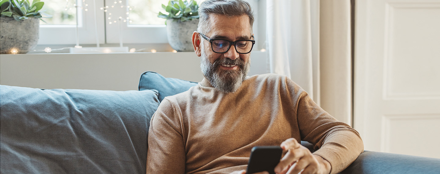 Man sitting on his couch looking up information on his mobile phone