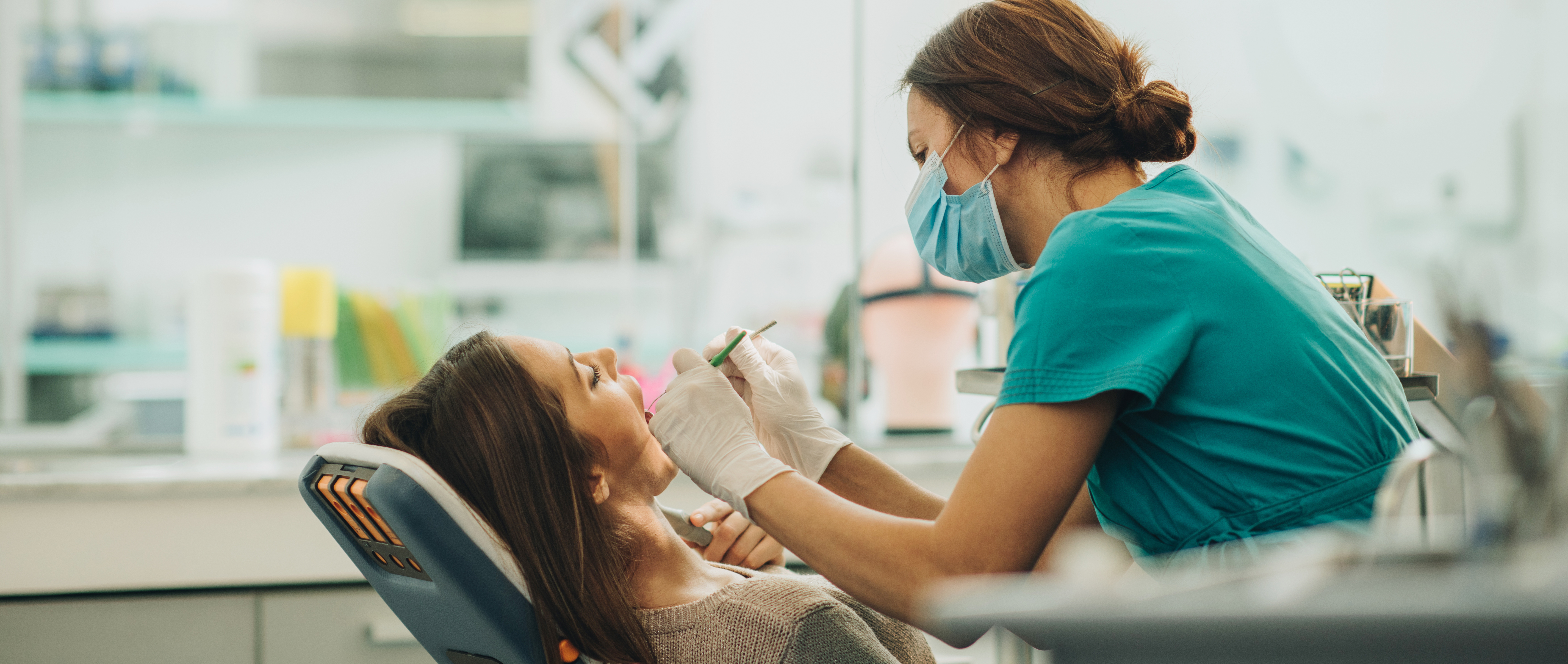 Woman lays back in a dental exam chair with her mouth open as a dental hygienist works on cleaning her teeth.