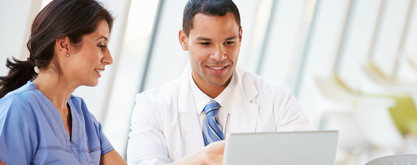 Dentist and hygienist sitting at a table reviewing records on a computer screen.